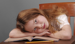 Young school girl putting head on desk, looking tired or bored