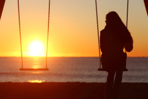 Single woman alone swinging on the beach and looking the other seat missing a boyfriend