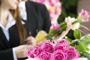 Mourning man and woman on funeral with pink rose standing at casket or coffin