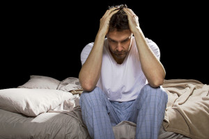 young man holding his head in his hands, unable sleep because of stress